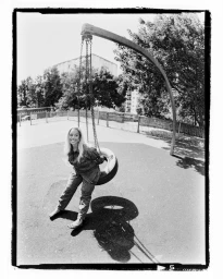 Jorja Smith sits smiling on a tire swing in an outdoor playground, captured in black and white with a film border.