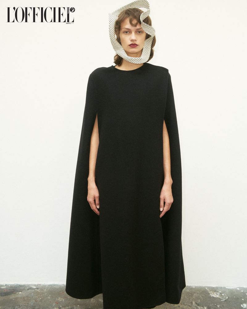 Woman in black dress and polka dot head covering posing in front of an off-white background in a fashion editorial shot.