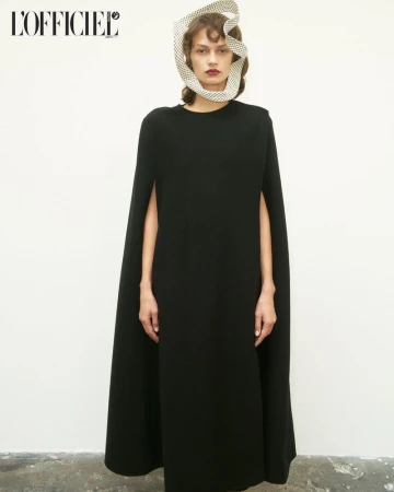 Woman in black dress and polka dot head covering posing in front of an off-white background in a fashion editorial shot.