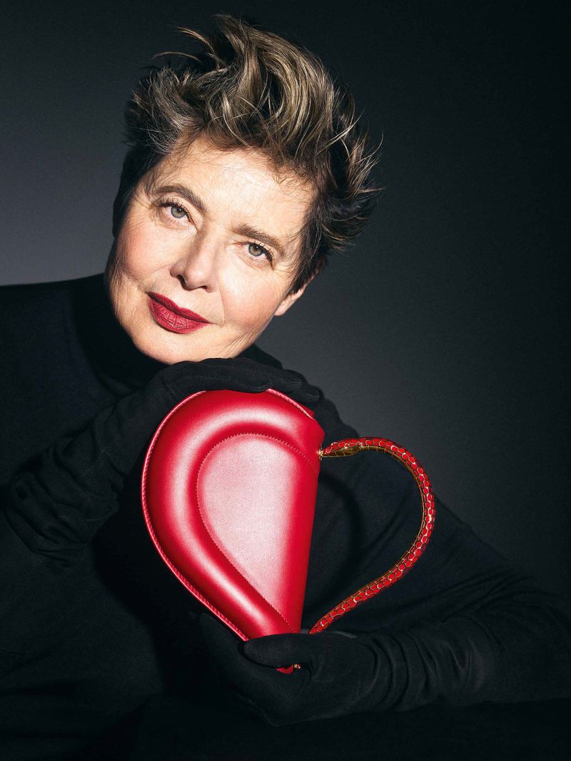 Portrait of an adult woman posing with a red, heart-shaped purse against a dark gradient background in a studio fashion setting.