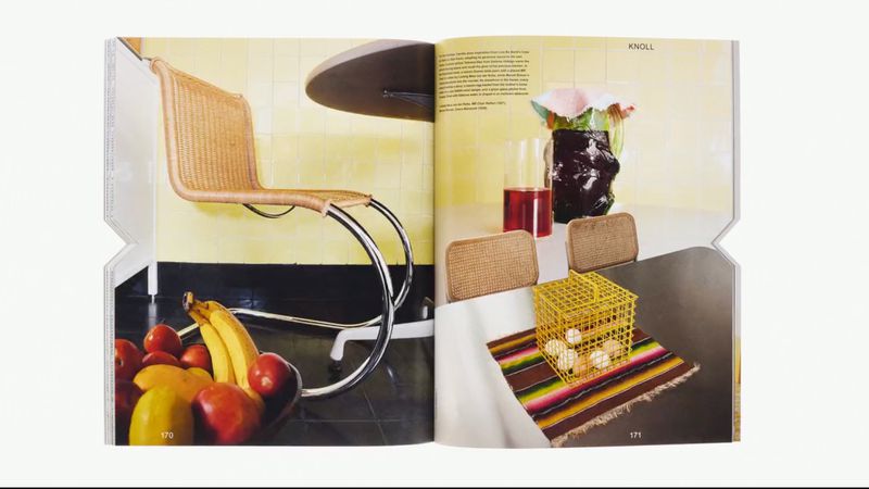 Magazine page showcases a still life of chairs, fruit, and decor elements in a retro-styled kitchen interior with yellow and black tiling.
