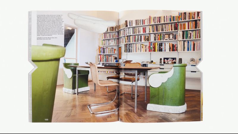 Interior shot of a room with bookshelves, a table, and chairs, taken from a magazine spread. Books and a green vase add color.