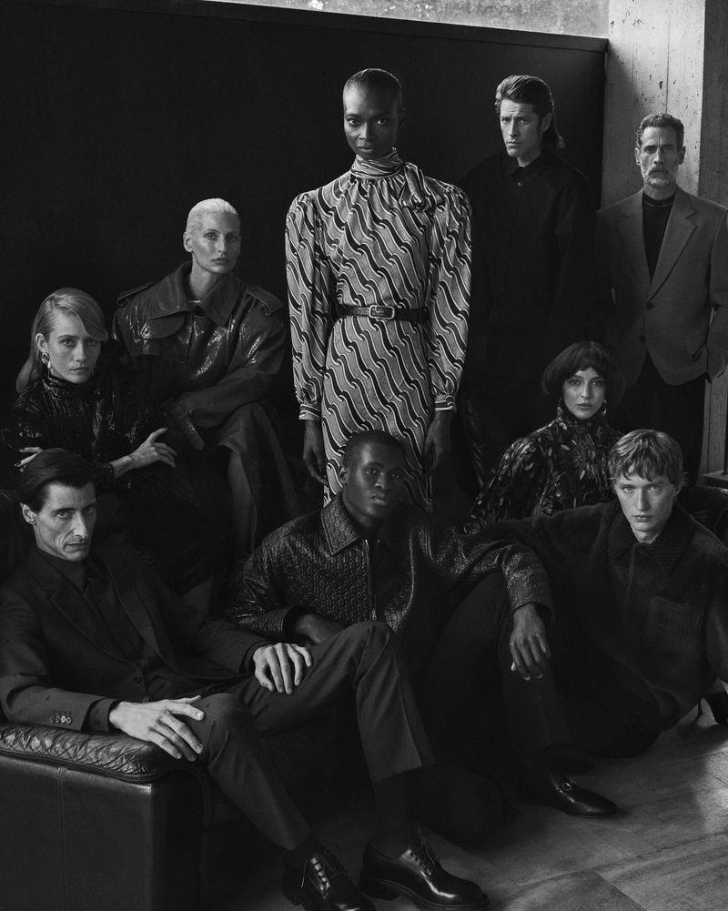 A group of nine fashion models poses indoors with black and white palette and artful composition, showcasing clothing and unique hairstyles.