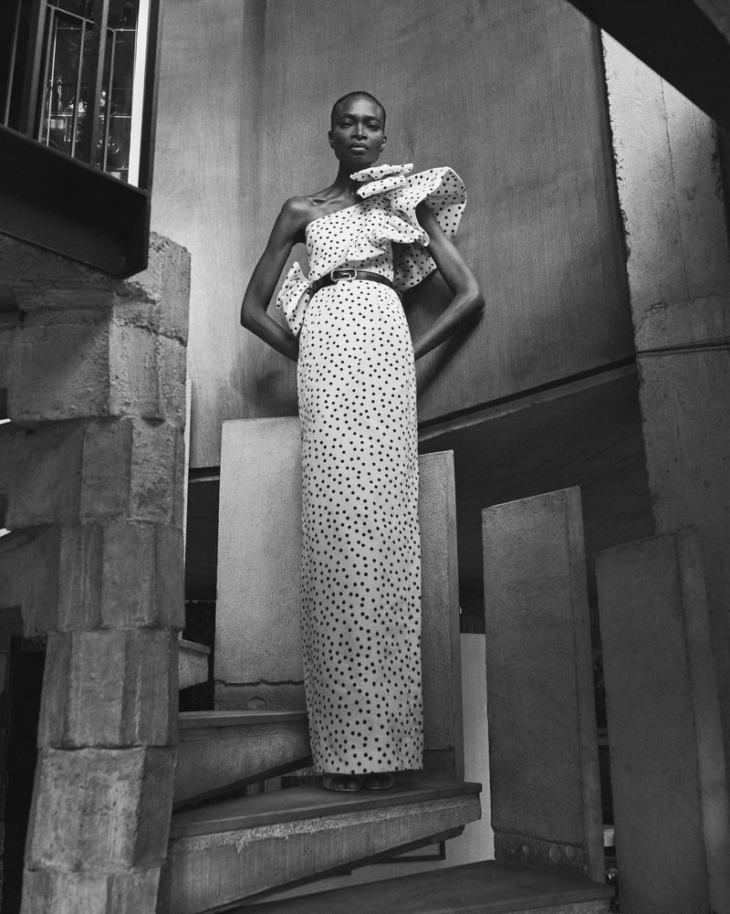 Elegant Black female fashion model poses on concrete stairs in a black and white studio shot wearing a polka dot, one-shoulder gown.