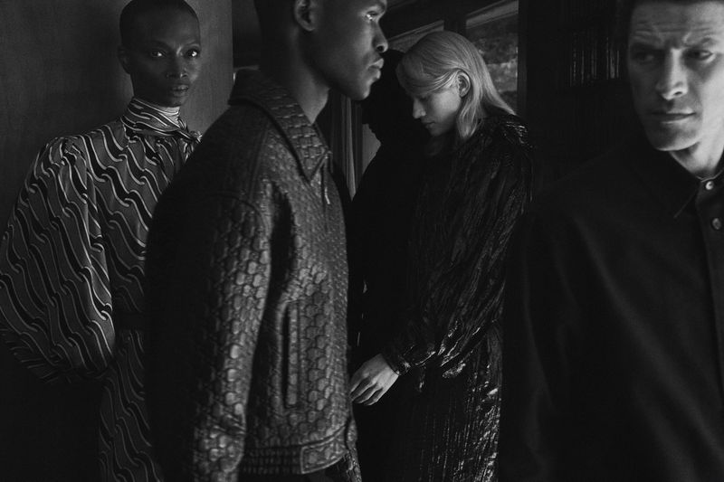Black and white fashion photo featuring a group of four people wearing stylish shirts and jackets in an indoor environment.