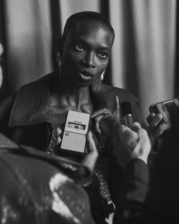 Black and white portrait of an adult female being interviewed with microphones and an audio recorder by reporters in an indoor space.