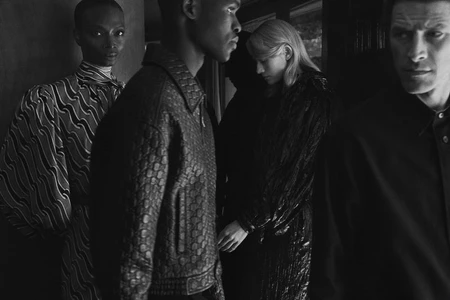Black and white editorial portrait of four diverse models in dark textured clothing gathered indoors