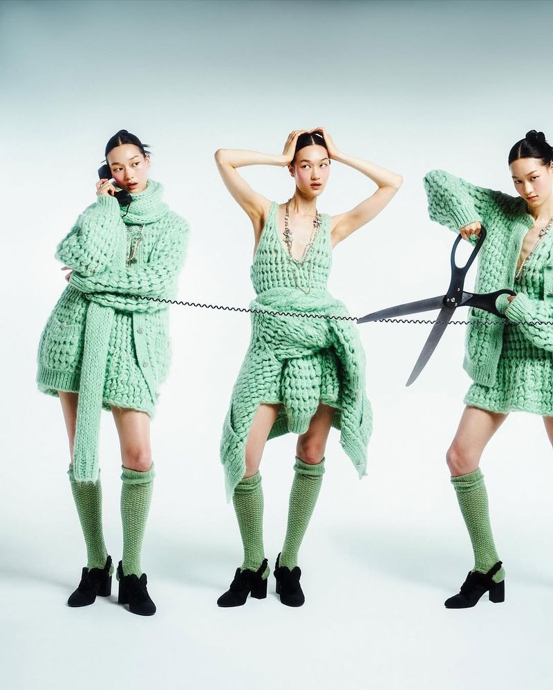 Three women in matching green knitwear, one on the phone, another with hands on her head, and another cutting a phone cord.