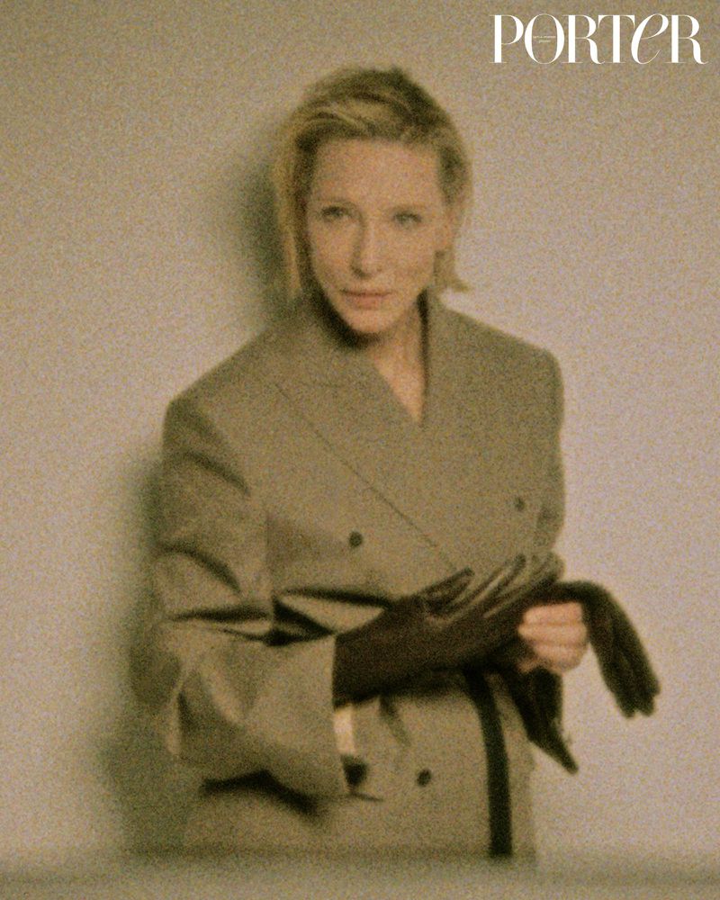 Editorial portrait of a blond woman in a blazer, posed in front of a neutral wall with the Porter magazine logo in the upper corner.