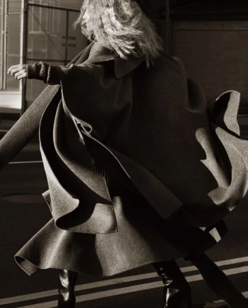 Woman in motion wearing oversized coat and black boots on a street in an editorial fashion photograph, capturing movement and style.