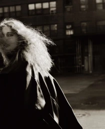 Apolline Rocco Fohrer in an oversized black leather jacket with windblown hair looking over her shoulder on a city street.