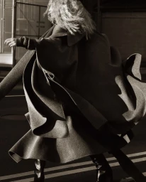 Model in a sweeping dark wool coat walking outdoors with motion blur in a fashion editorial for Harper's Bazaar U.S.
