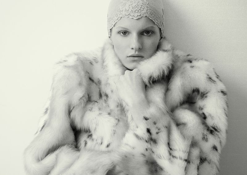 Monochrome portrait of a fair-skinned adult female wearing a fur coat and lace cap, posing against a white background, with a serious facial expression.