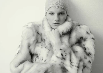 Model wearing a patterned fur coat and lace cap against a plain light background