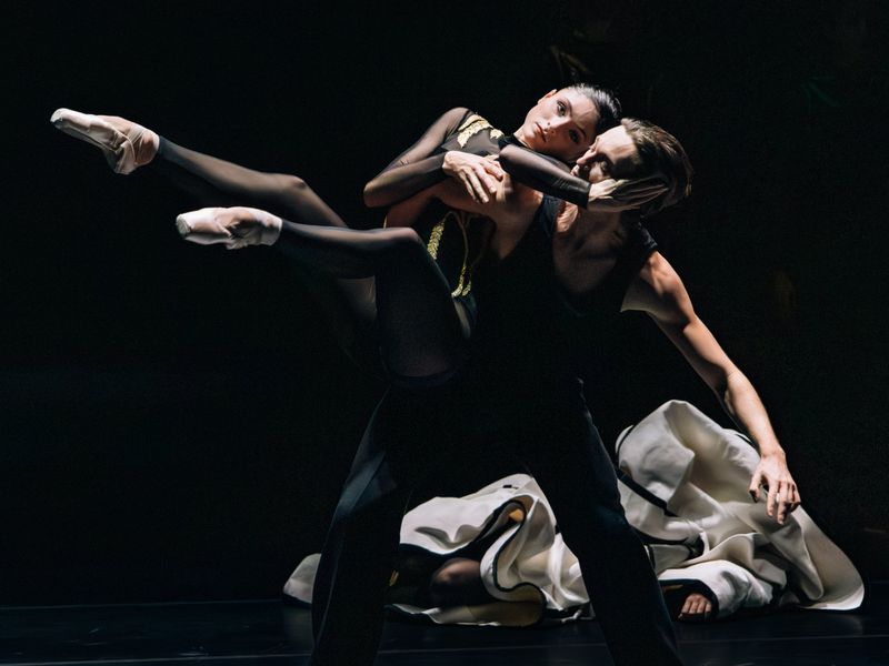 Dynamic ballet performance featuring two dancers, one male and one female, in black costumes against a dark stage backdrop.