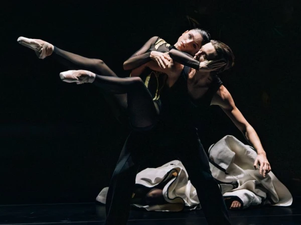 Dynamic ballet performance featuring two dancers, one male and one female, in black costumes against a dark stage backdrop.