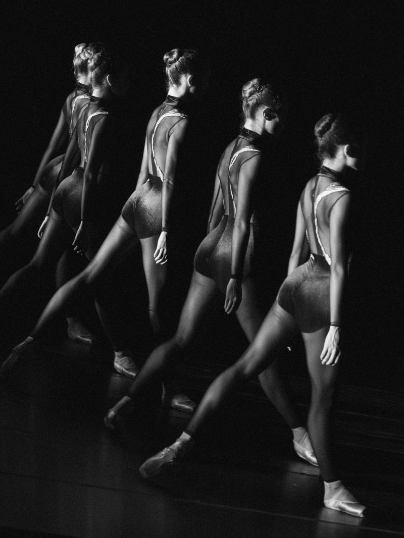 Black and white photo of a young female ballet dancer captured in a sequence of motion, highlighted against a dark background.