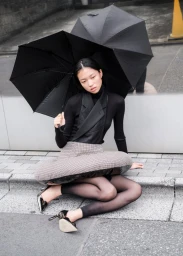 Model seated on a stone pavement holding a black umbrella under the Parallel project for Also Journal