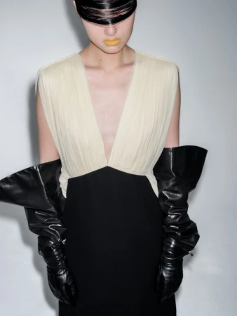 Woman in a modern black and white dress with high black shiny gloves poses against a bright white background in a studio fashion shoot.