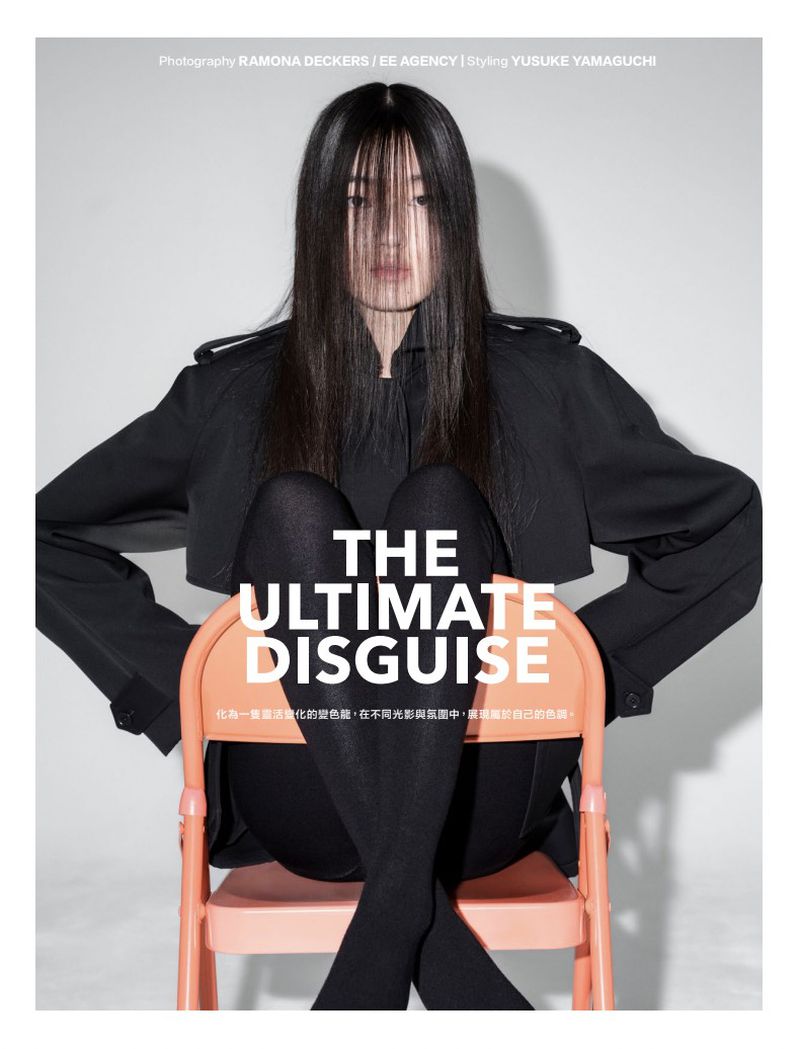 Fashion portrait of an Asian woman with long black hair sitting in an orange chair wearing a black jacket and tights in a studio.