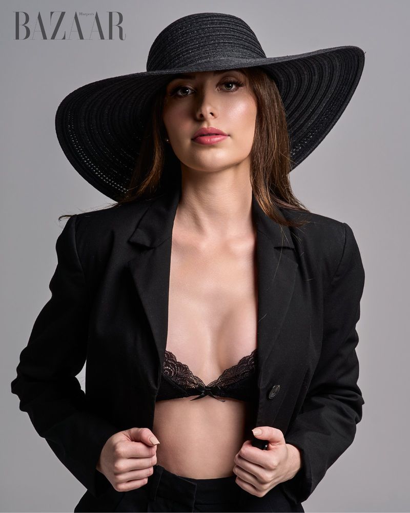 Portrait of a woman in a black hat and jacket, accessorized with a lace bra, in a studio setting for a fashion-forward editorial.