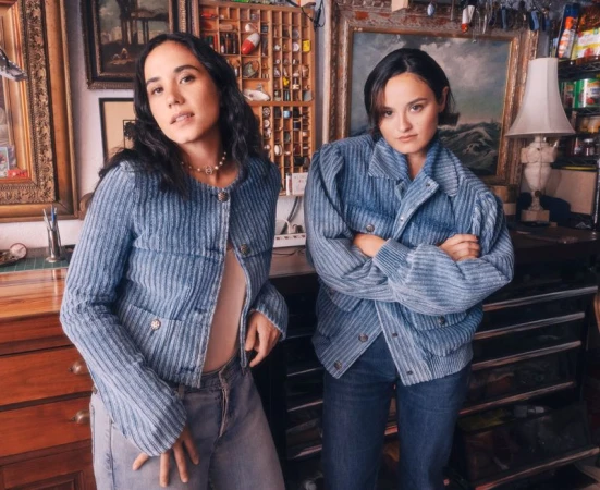 Chase and Jeannie Sui Wonders wearing matching light blue ribbed jackets in a room with framed artwork and a lamp.