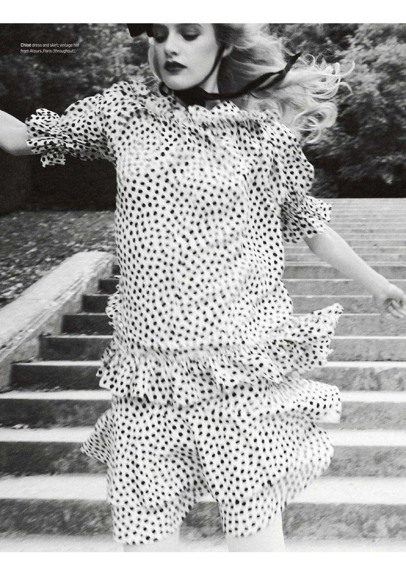 Monochrome fashion shot of a woman in a polka dot dress and black ribbon, set against a concrete staircase and foliage backdrop.