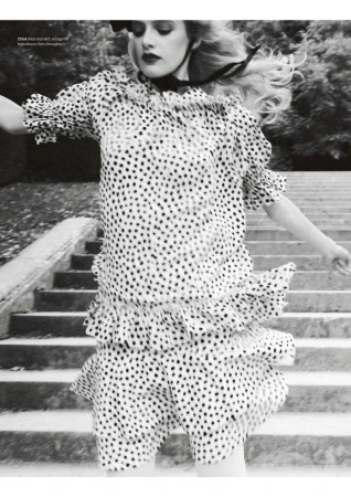 Monochrome fashion shot of a woman in a polka dot dress and black ribbon, set against a concrete staircase and foliage backdrop.
