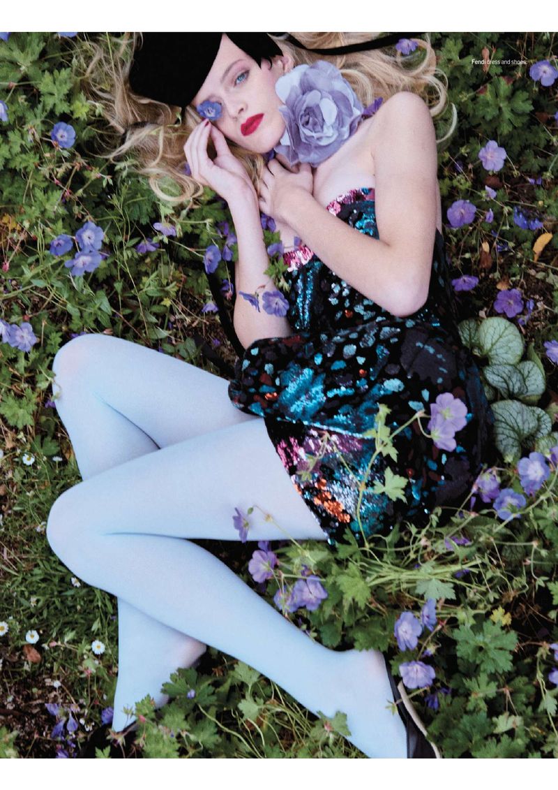Fashion shot of a woman lying on a meadow, wearing a sequined dress and light blue tights, accessorized with a rose and a hat.