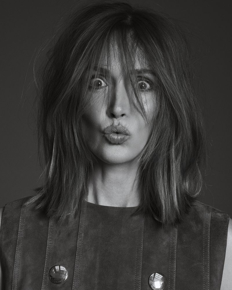 Black and white portrait of an adult woman with shoulder length hair making a kissing face, wearing a brown sleeveless top.