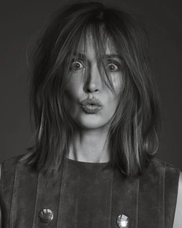 Black and white portrait of an adult woman with shoulder length hair making a kissing face, wearing a brown sleeveless top.