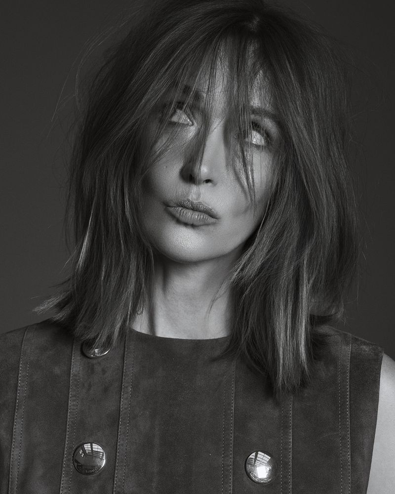 Monochrome portrait of a fair-skinned woman with shoulder-length hair, a sleeveless dress, and an expressive face, set against a plain backdrop.
