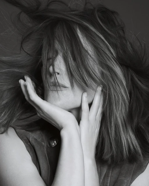 Monochrome portrait of a woman with flowing hair partially covering her face, hands gently touching her face, soft lighting.