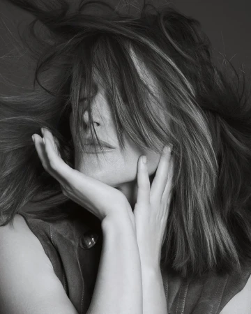 Portrait of actor Rose Byrne with tousled hair blowing across her face, cupping her chin with both hands.