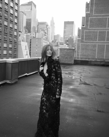 A woman in a black lace gown poses on a rooftop with a cityscape in the background, creating a striking black-and-white fashion image.