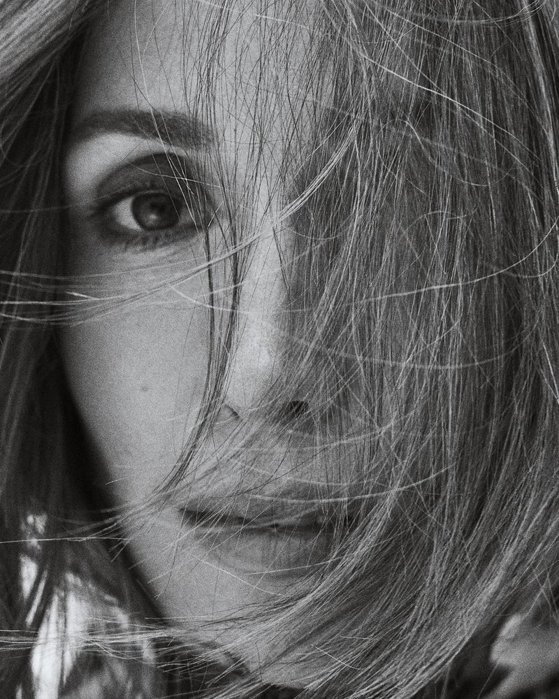 Close-up black and white portrait of an adult woman with fair skin and light hair partially obscuring her face and eye.