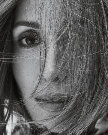 Close-up black and white portrait of an adult woman with fair skin and light hair partially obscuring her face and eye.
