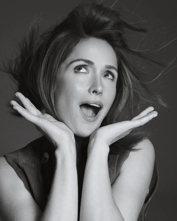 Portrait of a happy woman with wind-blown hair, hands framing face, looking upward against a neutral background in black and white.