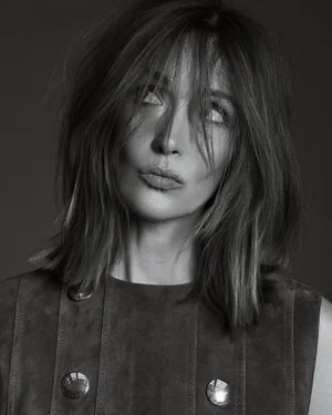 Portrait of actress Rose Byrne with tousled hair wearing a buttoned dark dress against a dark background