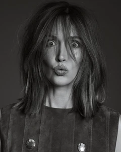 Black and white close-up portrait of actor Rose Byrne with tousled bangs puckering her lips in a sleeveless buttoned top.