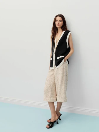Model wearing a black vest and light patterned culottes posing against a plain wall with a light blue floor.