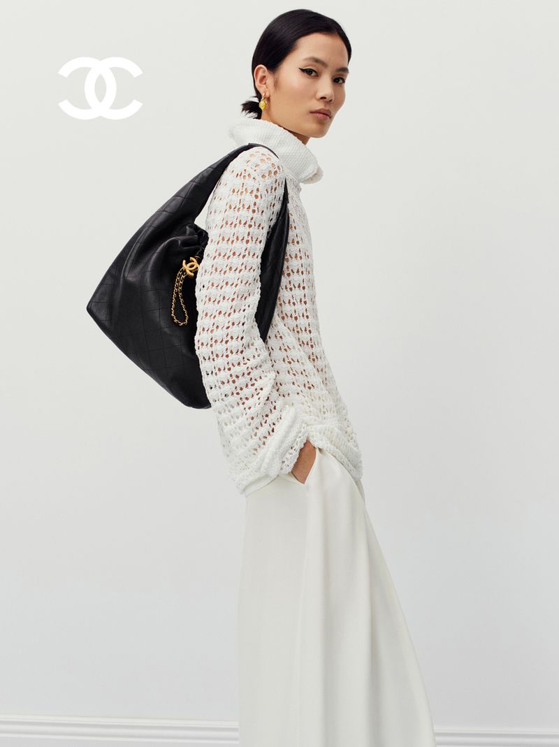 Fashion shot featuring an Asian woman wearing a white top and pants, accessorized with a black leather handbag and golden earrings.