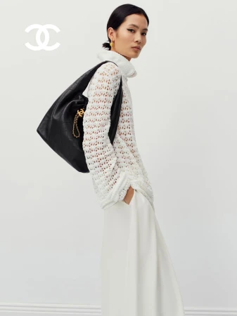Haojie Qi wearing a white open-knit turtleneck sweater and carrying a black quilted leather shoulder bag for Chanel.