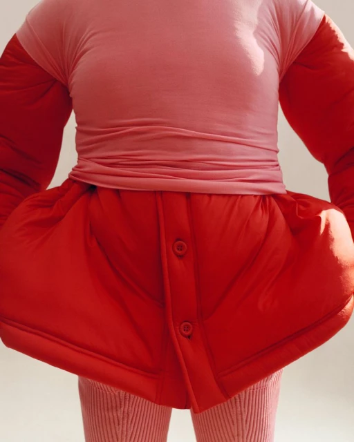Torso view of an adult female wearing a light pink top, large red skirt with button details, and striped leggings, with a neutral background.