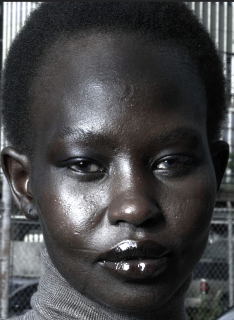 Close-up portrait of model Aweng Ade-Chuol wearing a high-neck grey top against an urban background