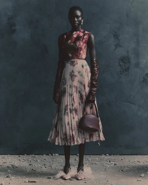 An adult African-American female model in floral dress and gloves poses in front of a mottled blue background in a full, eye-level shot.