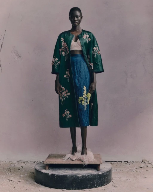 A striking fashion portrait features a Black woman in a floral robe and blue skirt, standing on a platform with decorative feather shoes.