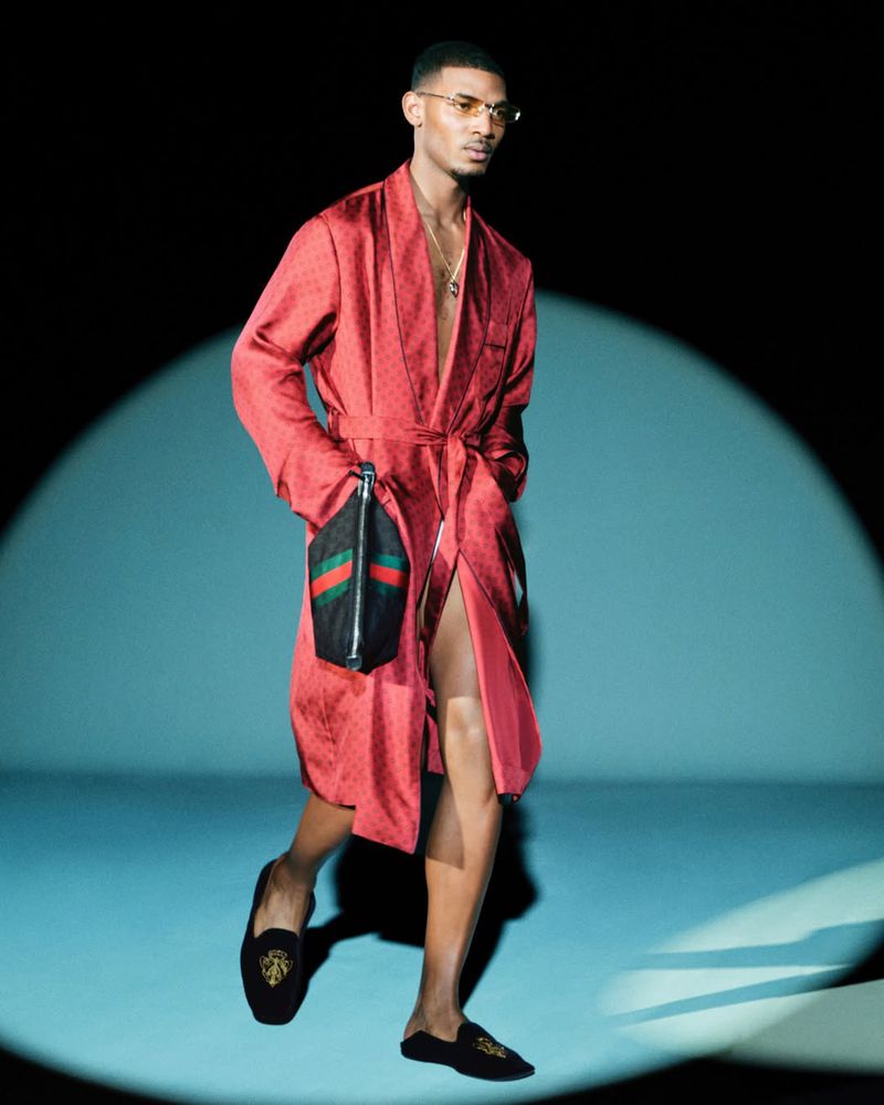 Model in red silk robe holding a handbag under spotlight against blue studio background for Gucci