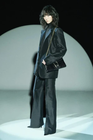 Woman in a black suit with a matching handbag posing against a spotlight, dark background, studio lighting, full-length shot, fashion shoot.