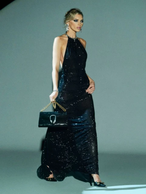 Elegant woman in a black sequin gown poses with a black handbag. Fashionable and stylish, showcasing an evening-wear look.